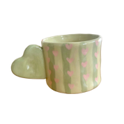 Taza de cerámica pintada a mano con asa de corazón, rayas verdes y corazones rosas.